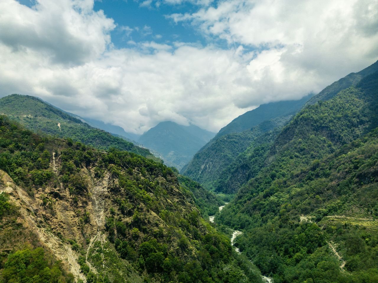 Home Lush green valley in Ghandruk with mountains and river under a cloudy sky in Nepal.